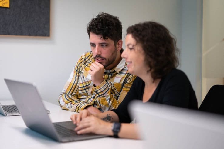 Foto mit 2 Personen am Tisch vor einem Laptop sitzend.